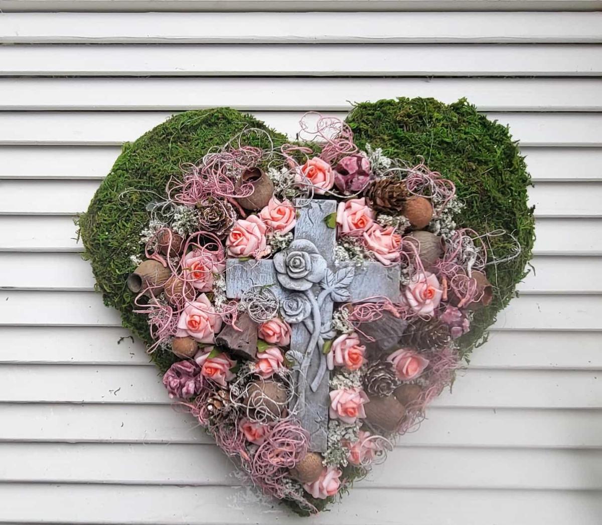 Grabherz aus Moos und vielen kleinen borrosafarbigen Rosen und einem großen Kreuz in der Mitte